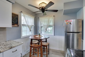 A kitchen with a round wooden table, two bar stools, a stainless steel refrigerator, and a ceiling fan. - Home w/ Fenced Yard, 13 Mi to Kansas City Stadium! (Kansas City)