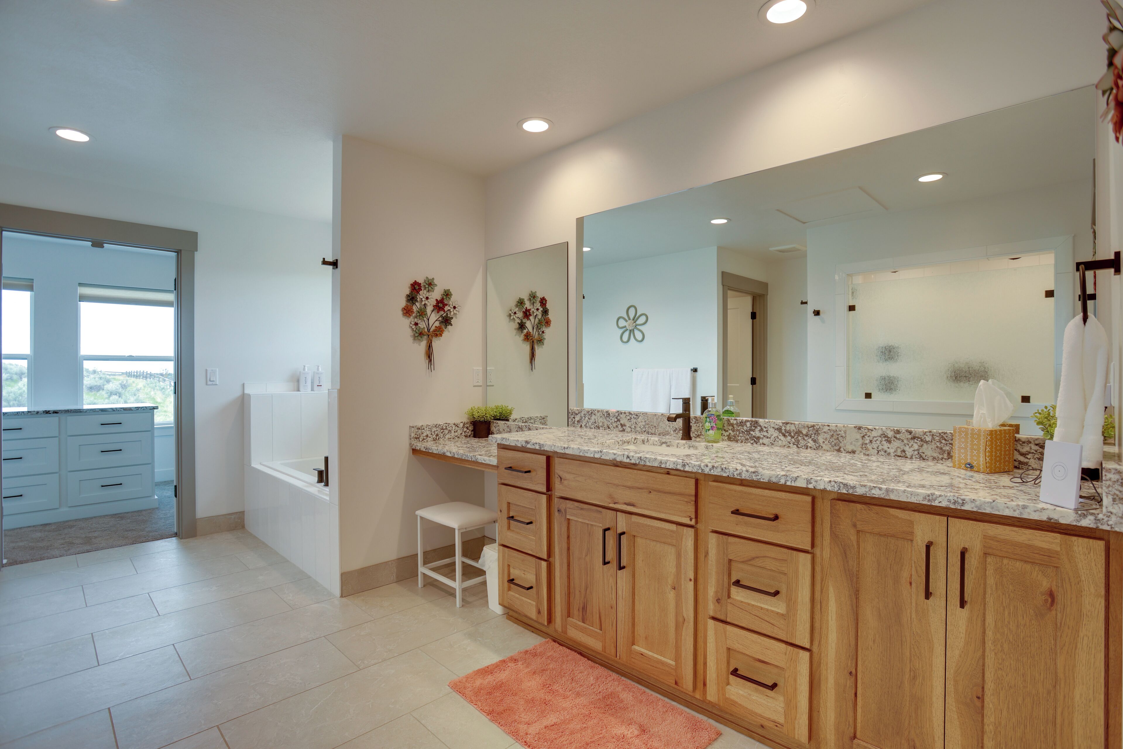 Un baño moderno con un espejo grande, armarios de madera, un lavabo blanco y un taburete pequeño.