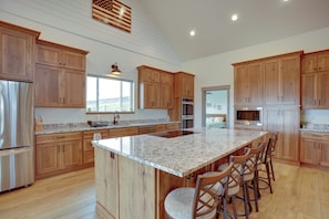 A kitchen with wooden cabinets, a granite countertop, stainless steel appliances, and a large island with bar stools. - Ultimate Family Getaway! Luxe 6BR Bear Lake Home (Garden City)