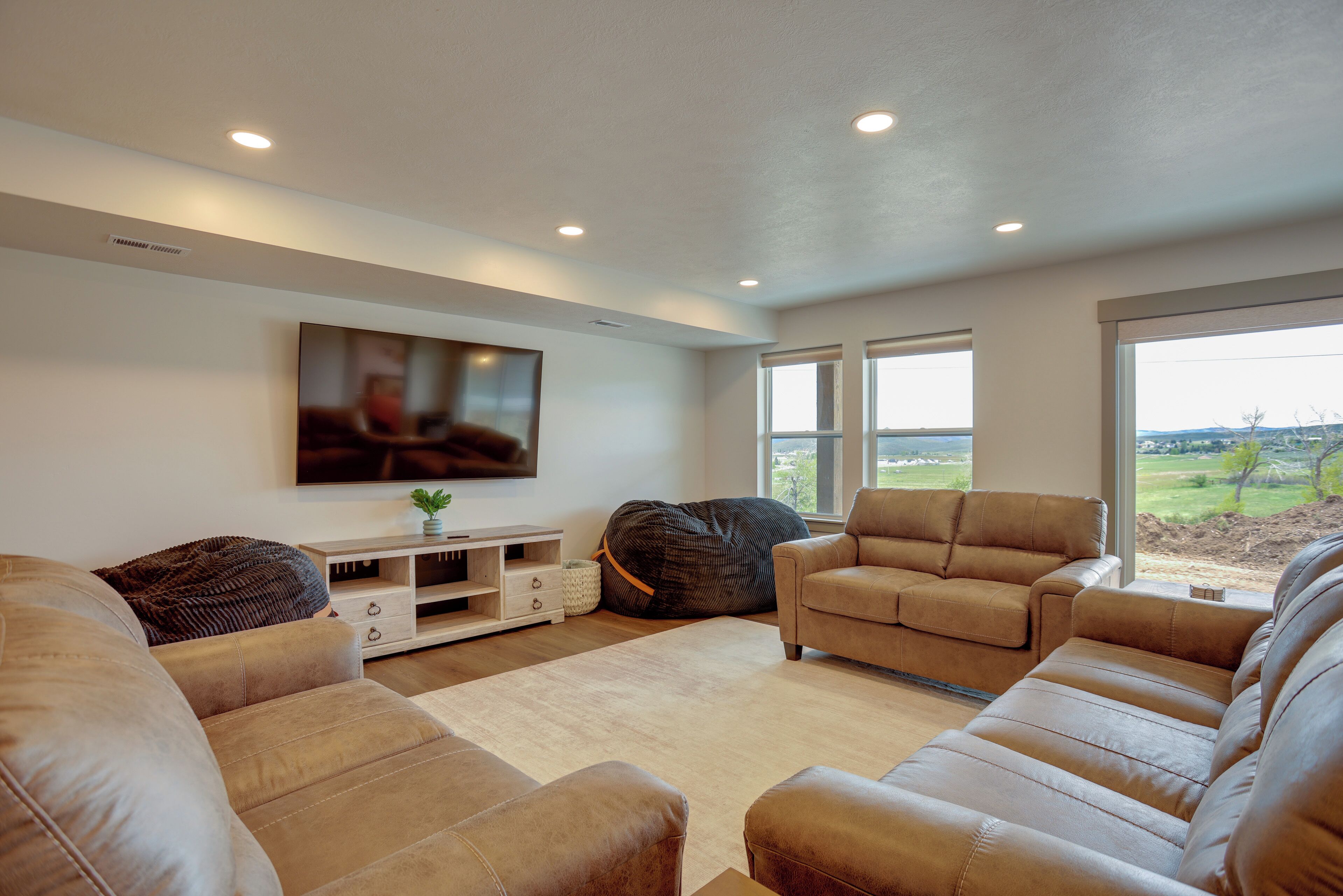 A living room with a flat-screen TV, beige sofas, a bean bag, and a large window with a view.