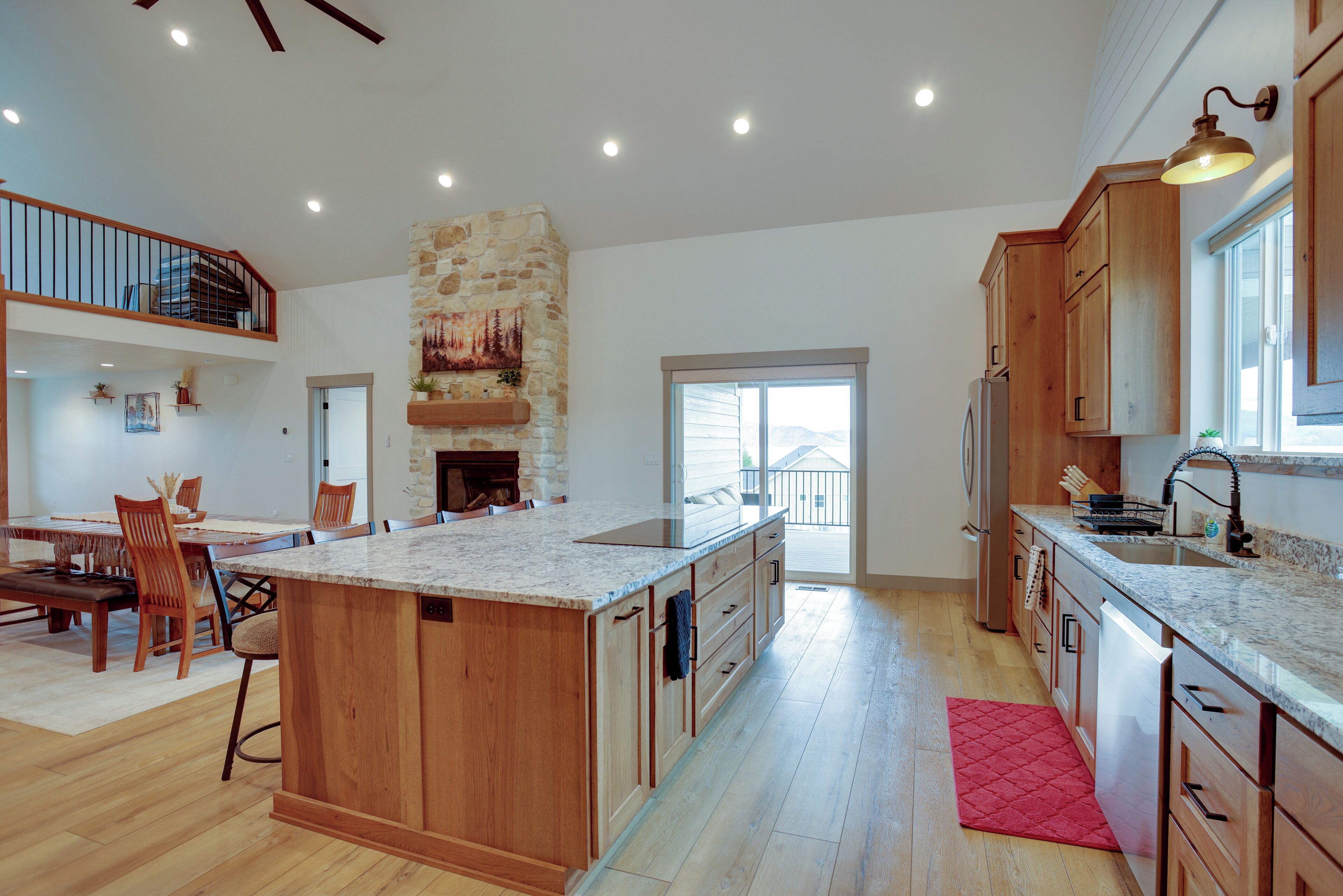 A spacious kitchen with a large island, wooden cabinets, and a stone fireplace.