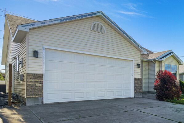 A single-story house with a white garage door, a brick foundation, and a small window on the upper floor.