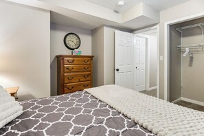 A bedroom with a bed, dresser, clock, and closet.