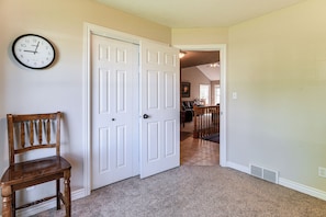 A hallway with a wooden chair, a white door, and a clock on the wall.