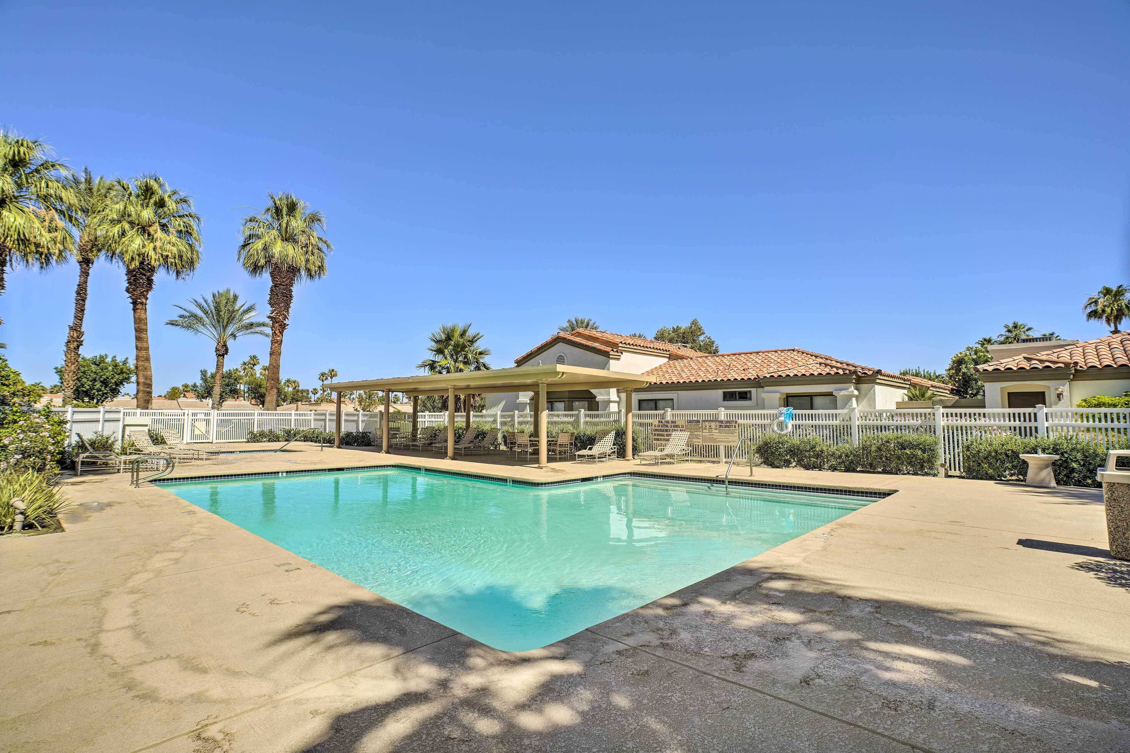 Una piscina con valla blanca, palmeras y un área de descanso cubierta.
