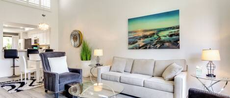 Una sala moderna con sofá, sillón, mesa de centro de vidrio y un comedor con sillas y mesa.