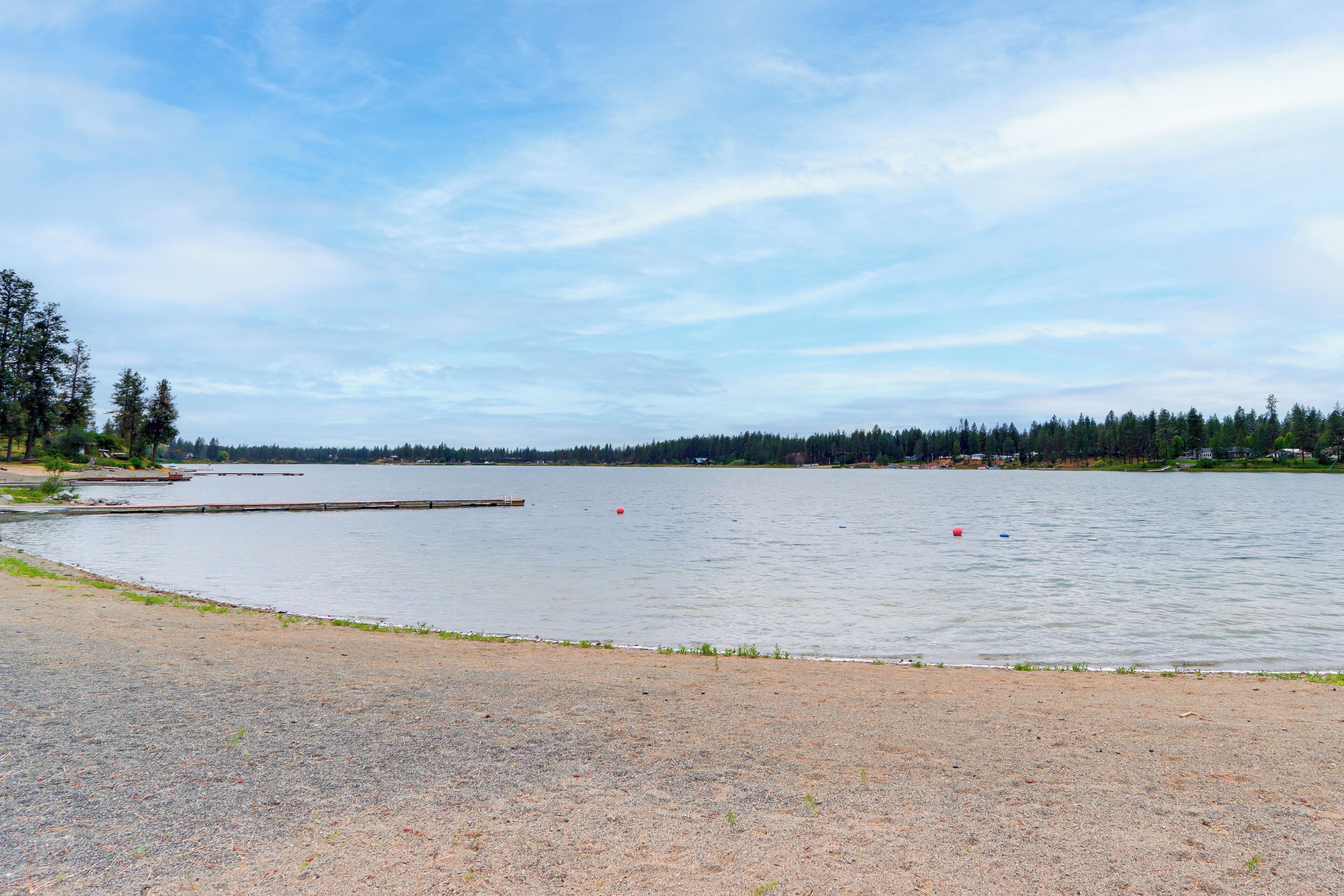A lakeside view with a dock, calm water, and a forested shoreline.