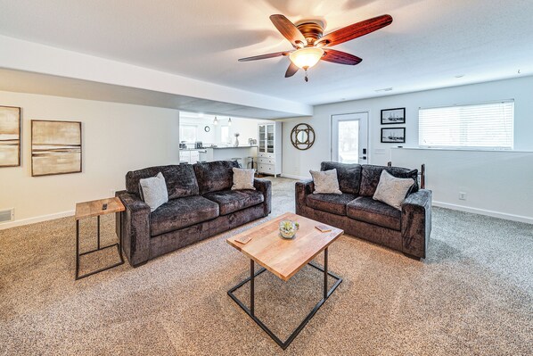A spacious living room with two dark sofas, a wooden coffee table, and a ceiling fan. - 4 Mi to K-state! Modern Garden-level Apt (Manhattan)