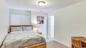 Un dormitorio con una cama de madera, una lámpara de noche, un cuadro enmarcado en la pared y una puerta a la derecha.