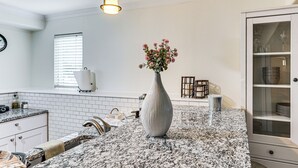 Una cocina con armarios blancos, encimera de granito, un florero con flores y una zona de comedor con sillas y una mesa.