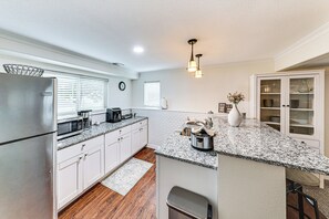 A kitchen with white cabinets, a granite countertop, a stainless steel refrigerator, a coffee maker, and a vase with flowers. - 4 Mi to K-state! Modern Garden-level Apt (Manhattan)