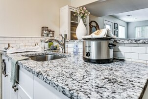 Una cocina con encimera de granito, una olla de acero inoxidable, un lavamanos y un armario blanco.