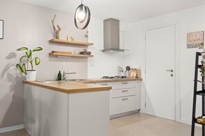 A modern kitchen with a central island, white cabinetry, a stainless steel range hood, and a hanging light fixture. - Pet friendly apartment Pergola in Poreč (Porec)