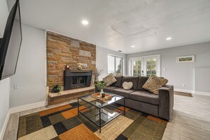 A living room with a stone fireplace, a sofa, a glass coffee table, and a large window. - Commute to Seattle! Comfortable Apt w/ Sunset View (Federal Way)
