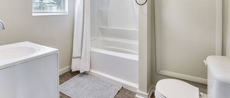 A bathroom with a bathtub, toilet, sink, and window with blinds.