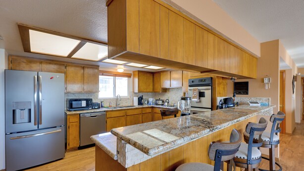 Una cocina moderna con armarios de madera, electrodomésticos de acero inoxidable, encimera de granito y taburetes de bar.