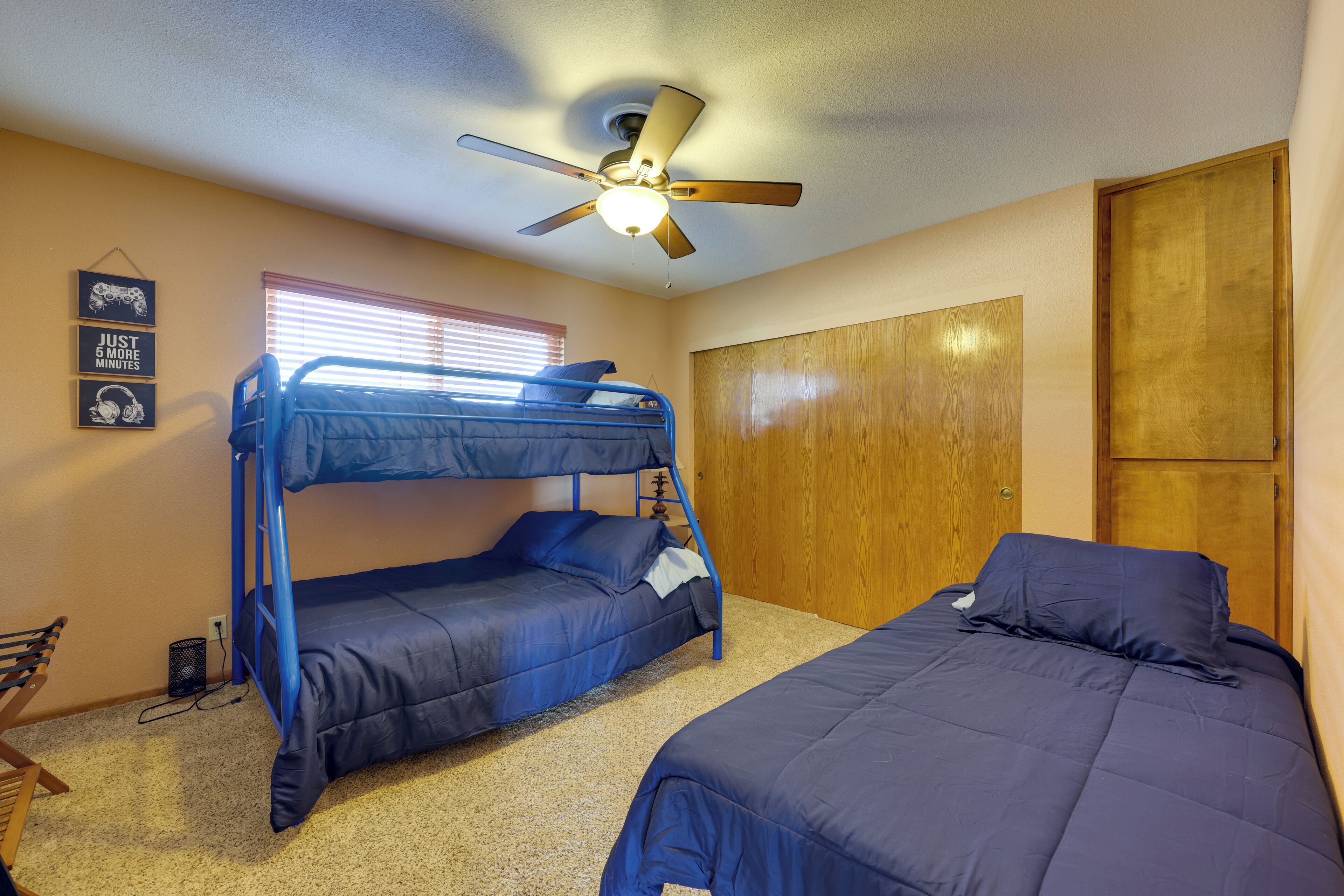Une chambre avec des lits superposés, un ventilateur de plafond, une porte en bois et une étagère fixée au mur.