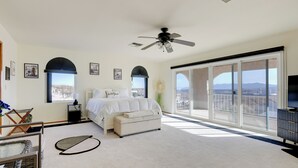 Un dormitorio con cama, ventilador de techo, una ventana grande y vista a la ciudad.