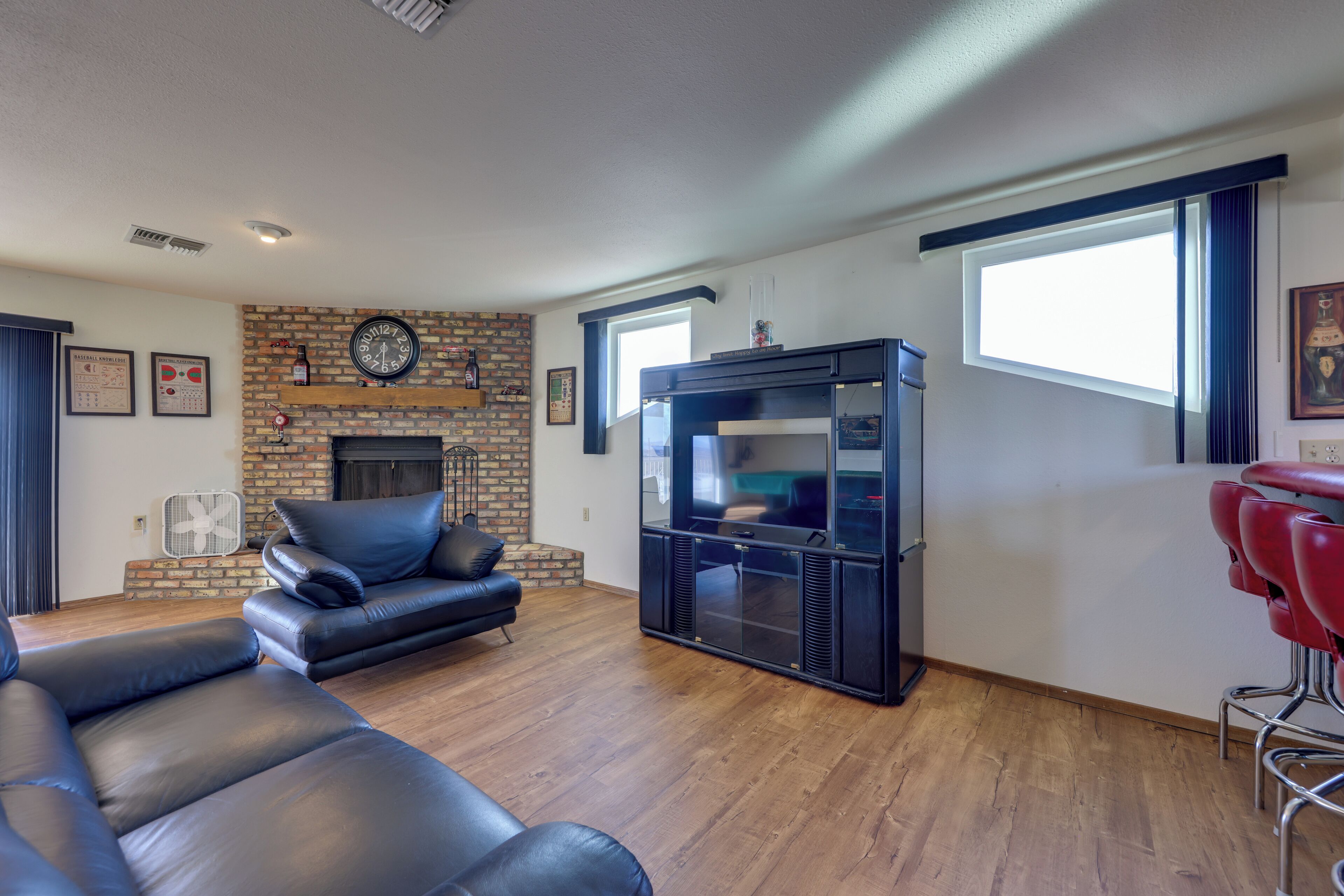 A living room with a brick fireplace, a large flat-screen TV, leather sofas, and a red bar stool.