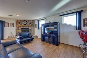 Una sala de estar con chimenea de ladrillo, un televisor de pantalla plana grande, sofás de cuero y un taburete de bar rojo.