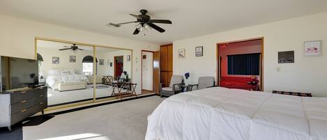A bedroom with a large bed, a ceiling fan, a mirror, a dresser, and a red door.