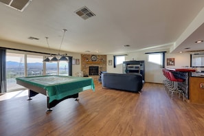 Amplia habitación con mesa de billar, chimenea, zona de bar y grandes ventanales con vistas.