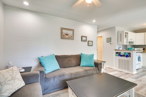 A living room with a sofa, a coffee table, and a kitchen area in the background. - Steps to Ocean! Family-friendly Carolina Beach Gem (Carolina Beach)