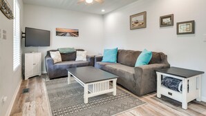 Ein Wohnzimmer mit Ecksofa, Couchtisch, Fernseher und Kunstwerken an der Wand.