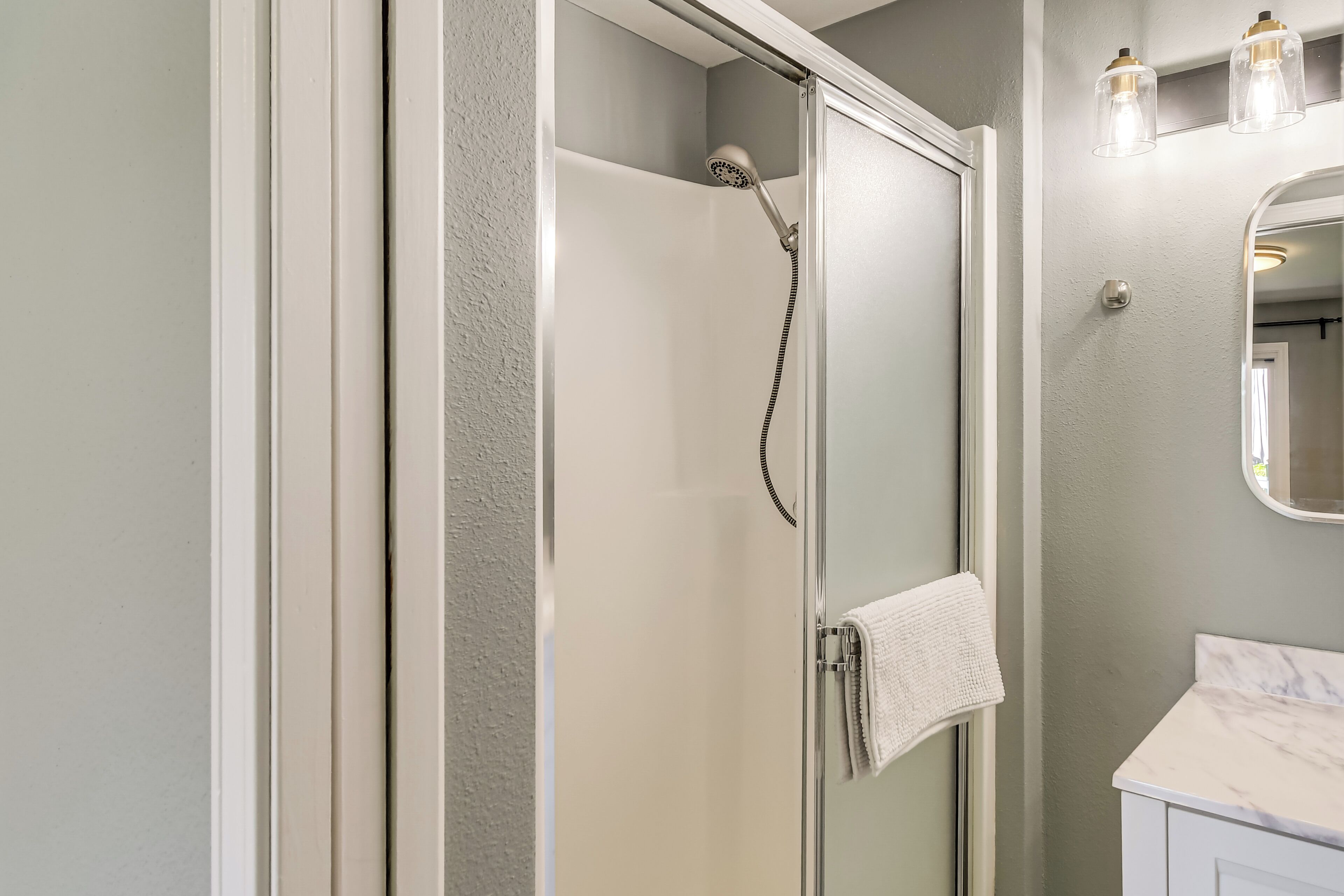A bathroom with a glass shower enclosure, a white vanity with a marble countertop, and a mirror with a gold frame.