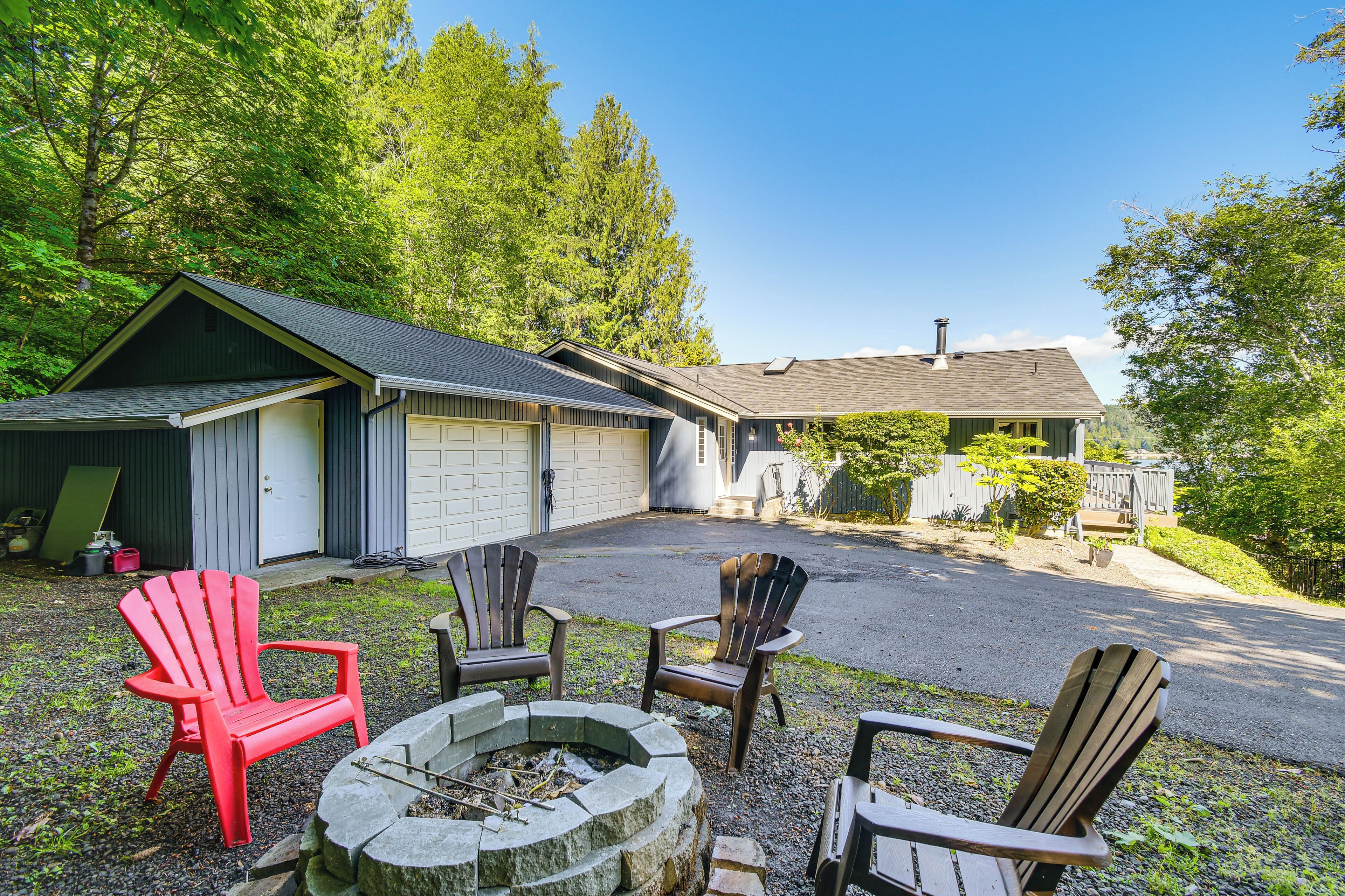Une maison avec un garage, un foyer extérieur et plusieurs fauteuils Adirondack.