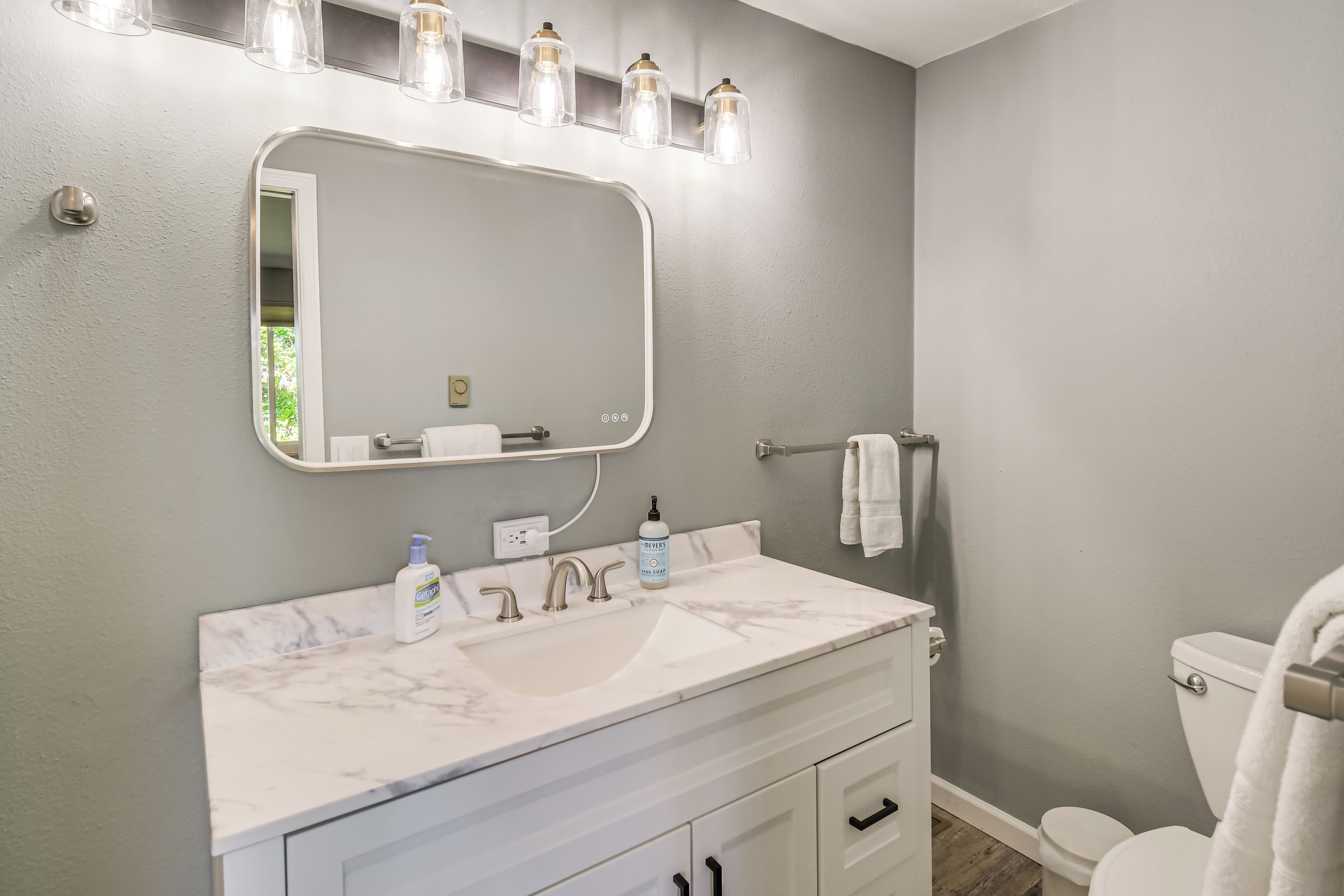 A bathroom with a marble sink, a large mirror, and a towel rack.