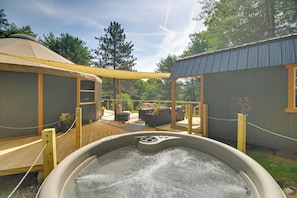 A hot tub, wooden deck, outdoor seating area, and a covered structure.