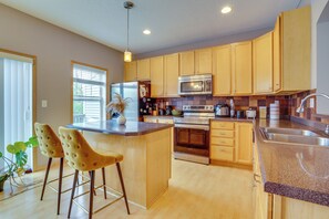 A modern kitchen with wooden cabinets, stainless steel appliances, and a central island with bar stools. - Spacious & Quiet Townhome In the Twin Cities (Roseville)