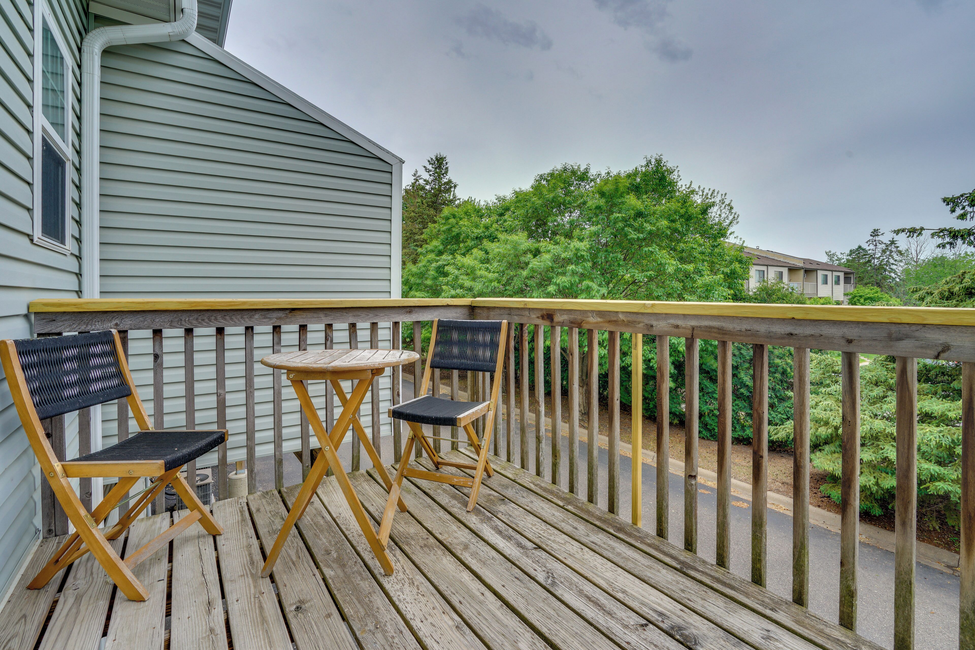 A wooden deck with two chairs and a small table, a railing, and a view of a house and greenery.
