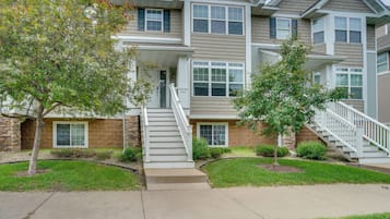A multi-story residential building with a central staircase, a front porch, and a well-maintained lawn.