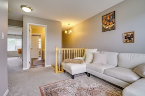 A living room with a white sofa, a patterned rug, a staircase, and a door leading to another room. - Spacious & Quiet Townhome In the Twin Cities (Roseville)