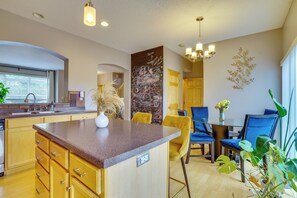 A modern kitchen with a granite countertop, wooden cabinets, and a dining area with blue chairs and a table. - Spacious & Quiet Townhome In the Twin Cities (Roseville)