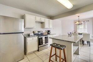 Eine moderne Küche mit weißen Schränken, einer Granit Arbeitsplatte, einem Edelstahlbackofen und einem Barhocker.