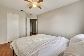 Ein Schlafzimmer mit einem Bett, einem Deckenventilator und einer Tür zu einem weiteren Raum.