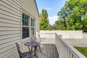 Une terrasse en bois avec une table et des chaises, une clôture blanche et des arbres en arrière-plan.