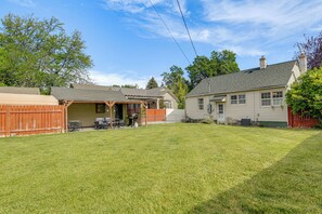 Un jardin à l’arrière d’une maison, avec une terrasse couverte, une clôture en bois et une maison dotée d’une cheminée.