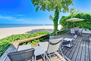 A wooden deck with outdoor furniture, a view of the beach, and a tree with green foliage. - Sun, Sand & Boating Fun! Extended Macatawa Getaway (Macatawa)