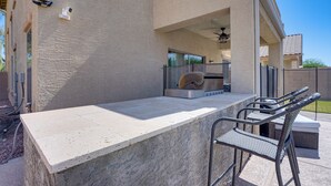 An outdoor bar area with a stone countertop, metal chairs, and a ceiling fan. - Modern Family Oasis Pool Game Room (Maricopa)