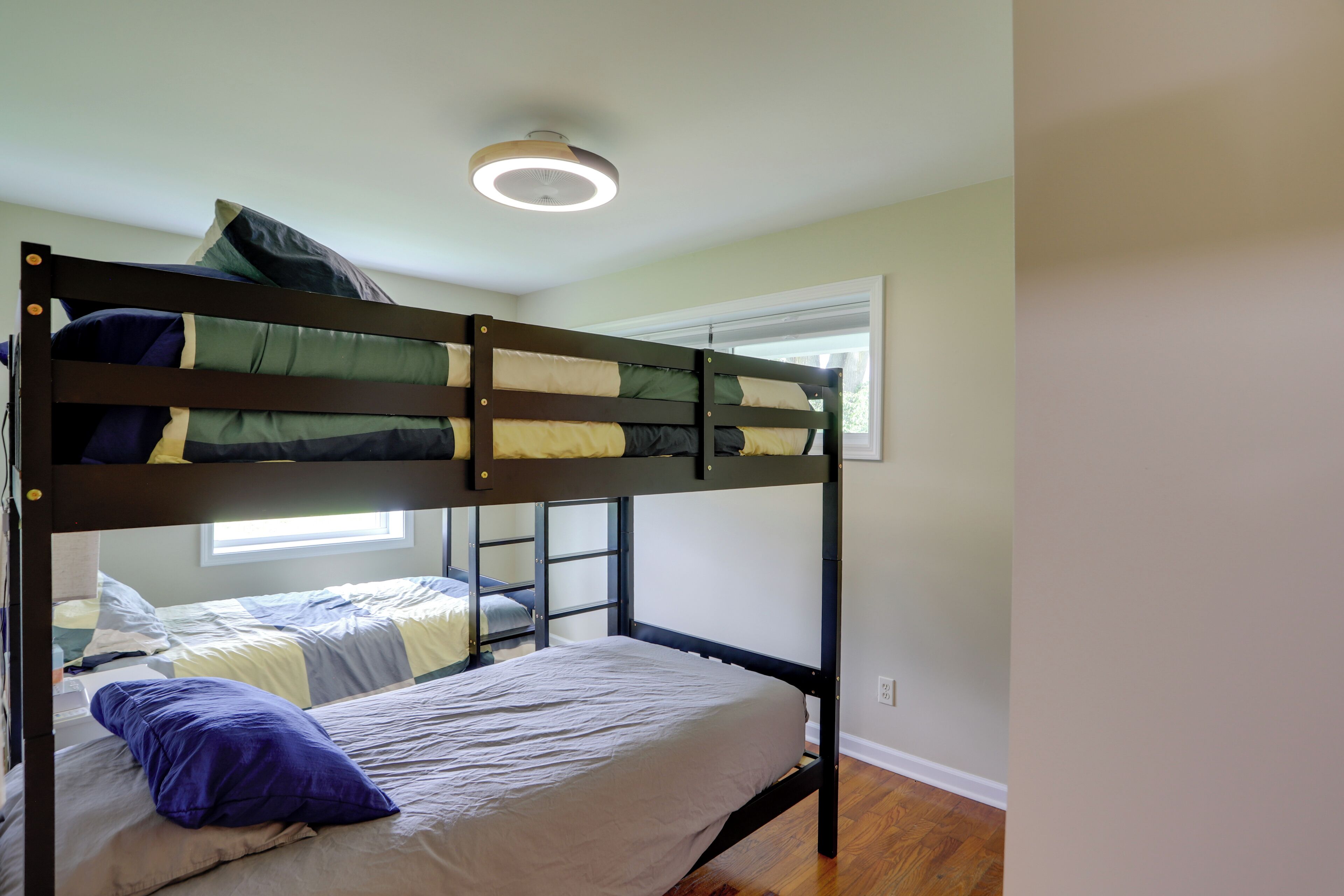 Une chambre avec un lit superposé, une fenêtre, un plancher en bois et un luminaire au plafond.