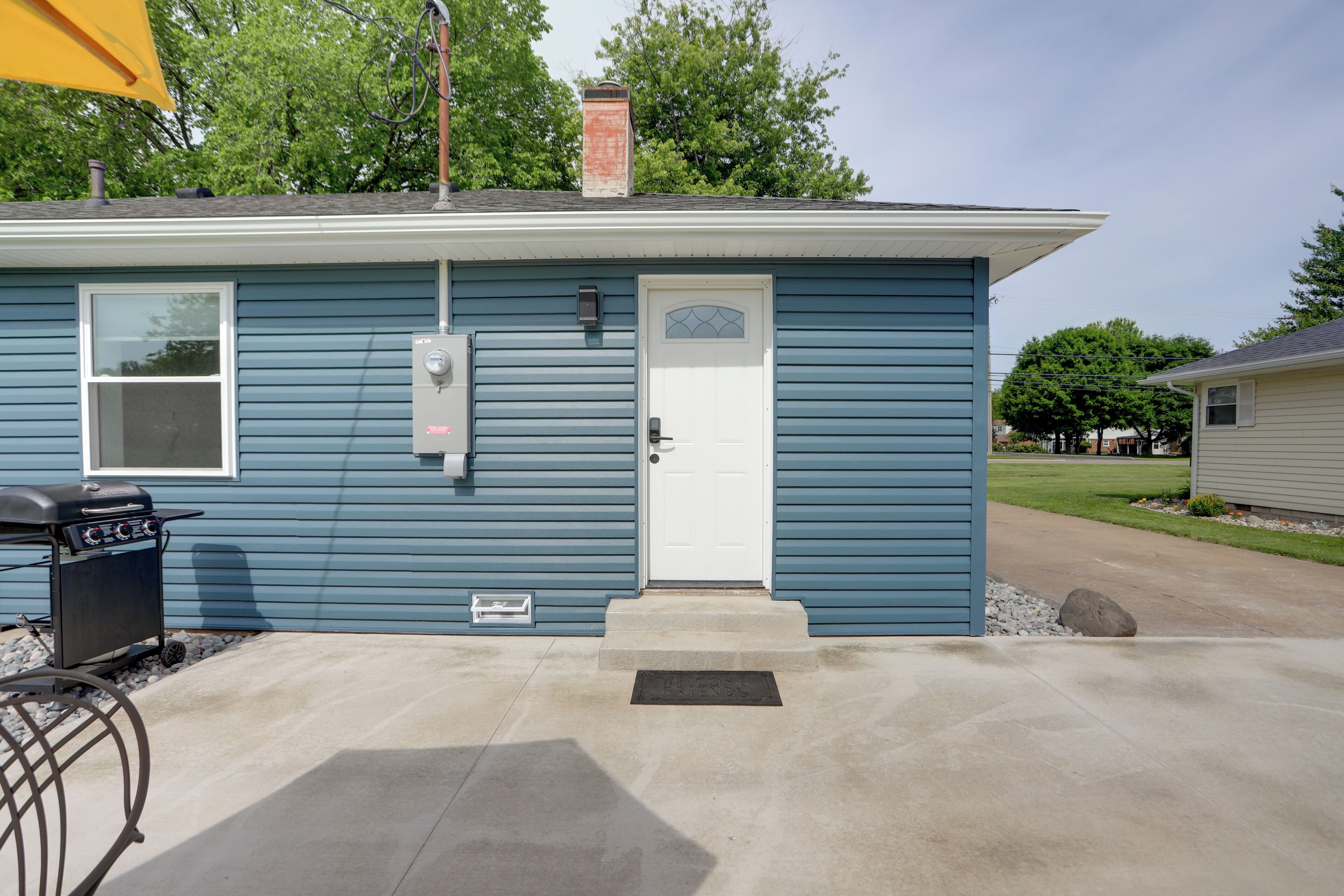 A residential house with a front door, a small window, a chimney, and a barbecue grill outside.