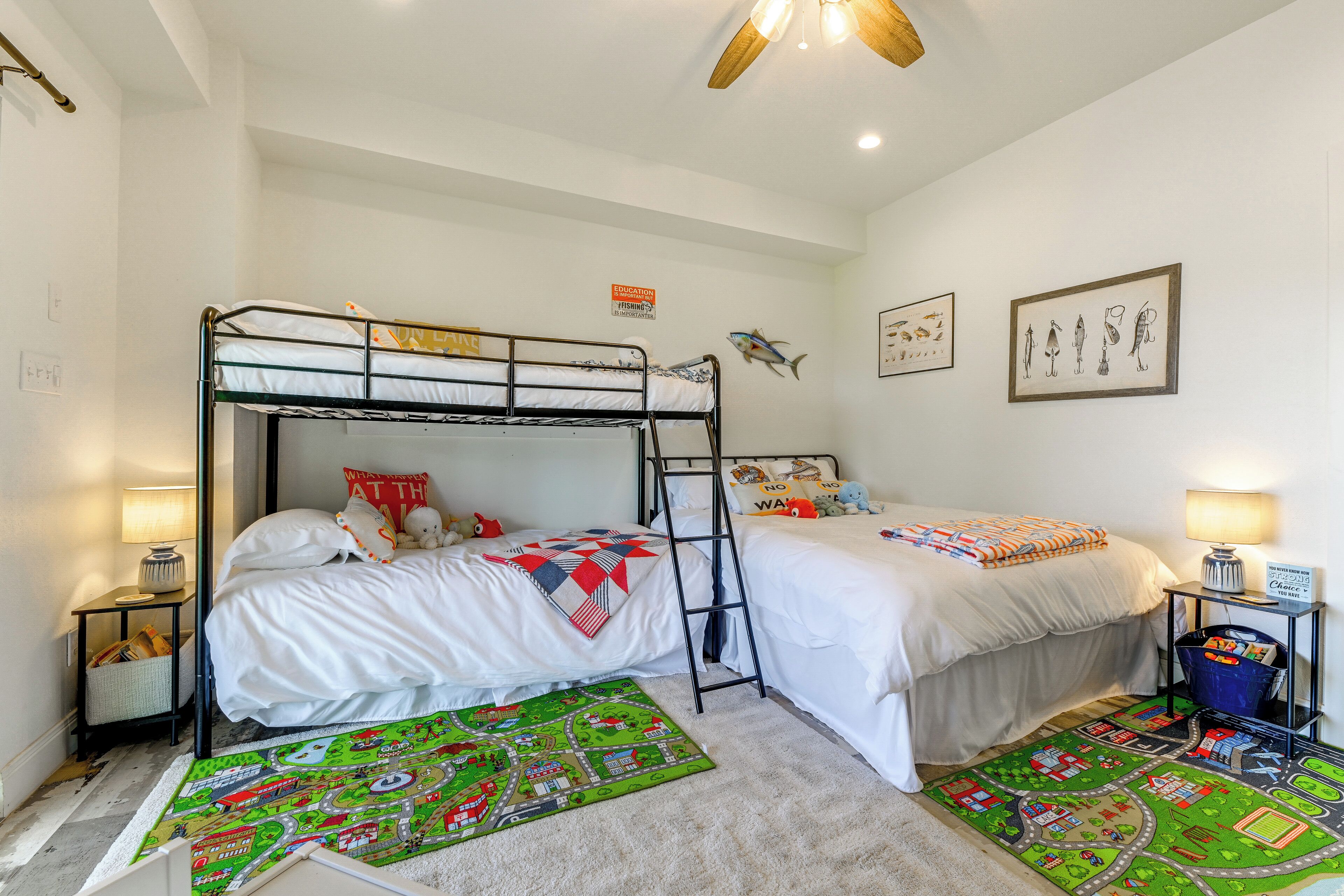 A bunk bed room with a ladder, two bedside tables with lamps, a wall with educational posters, and a colorful rug.