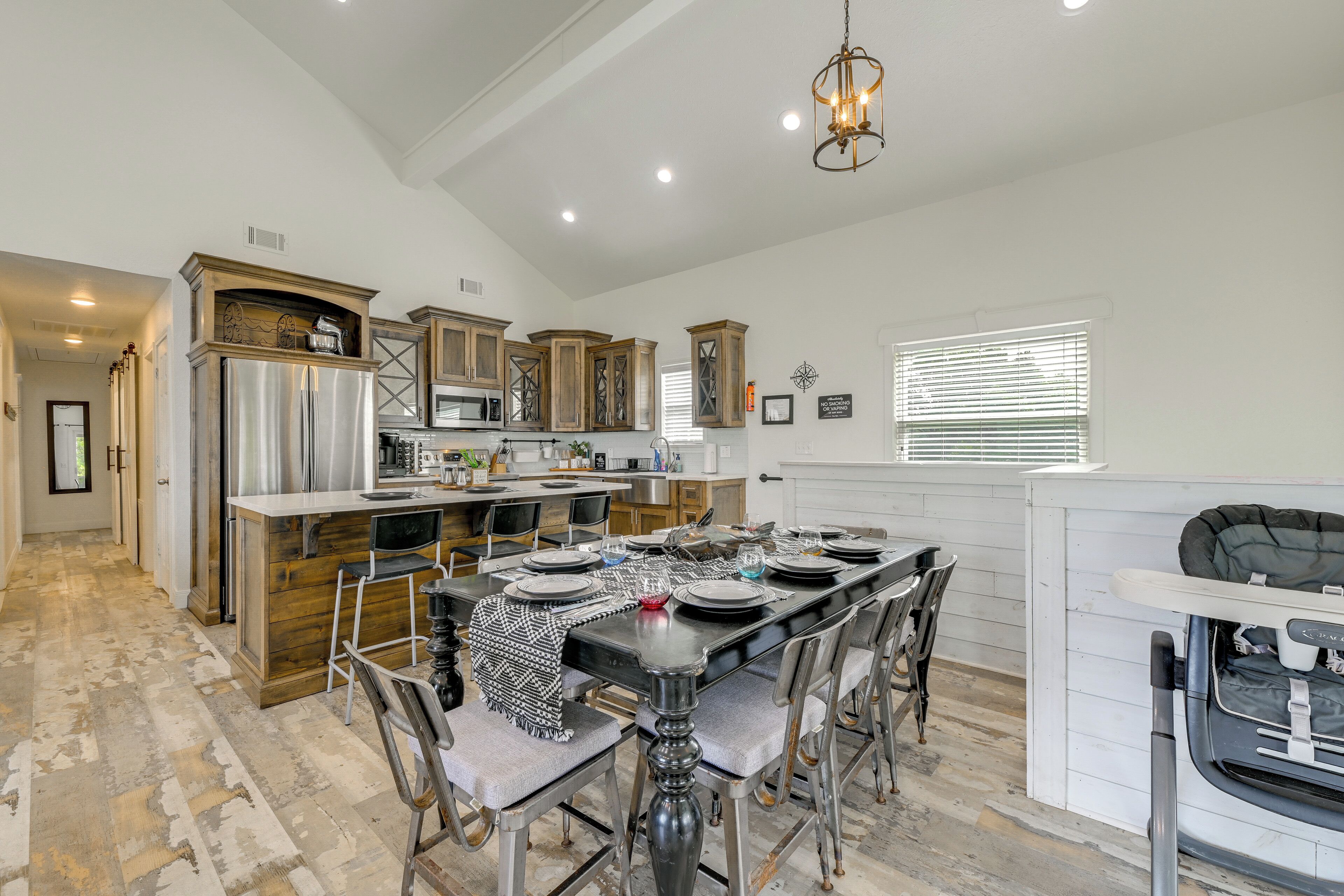 A spacious kitchen with a dining area, wooden cabinets, stainless steel appliances, and a chandelier.