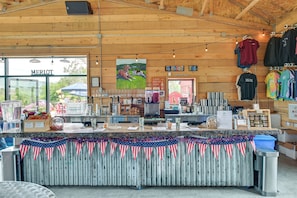 A rustic wooden interior with a counter displaying various items, a sign for 'MERLOT', and a view of the outdoors.