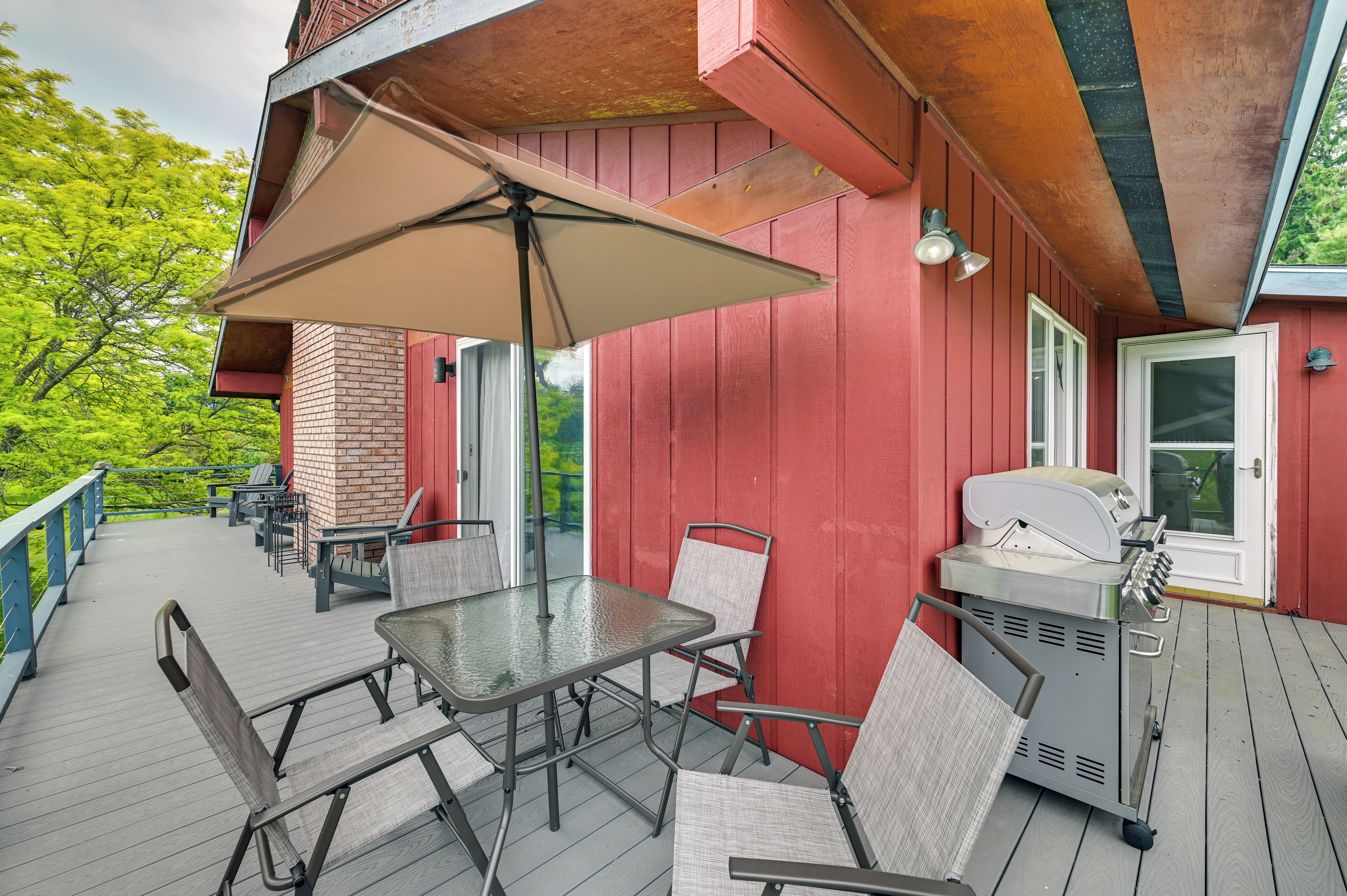 A covered outdoor patio with a table and chairs, a grill, and a red building in the background.