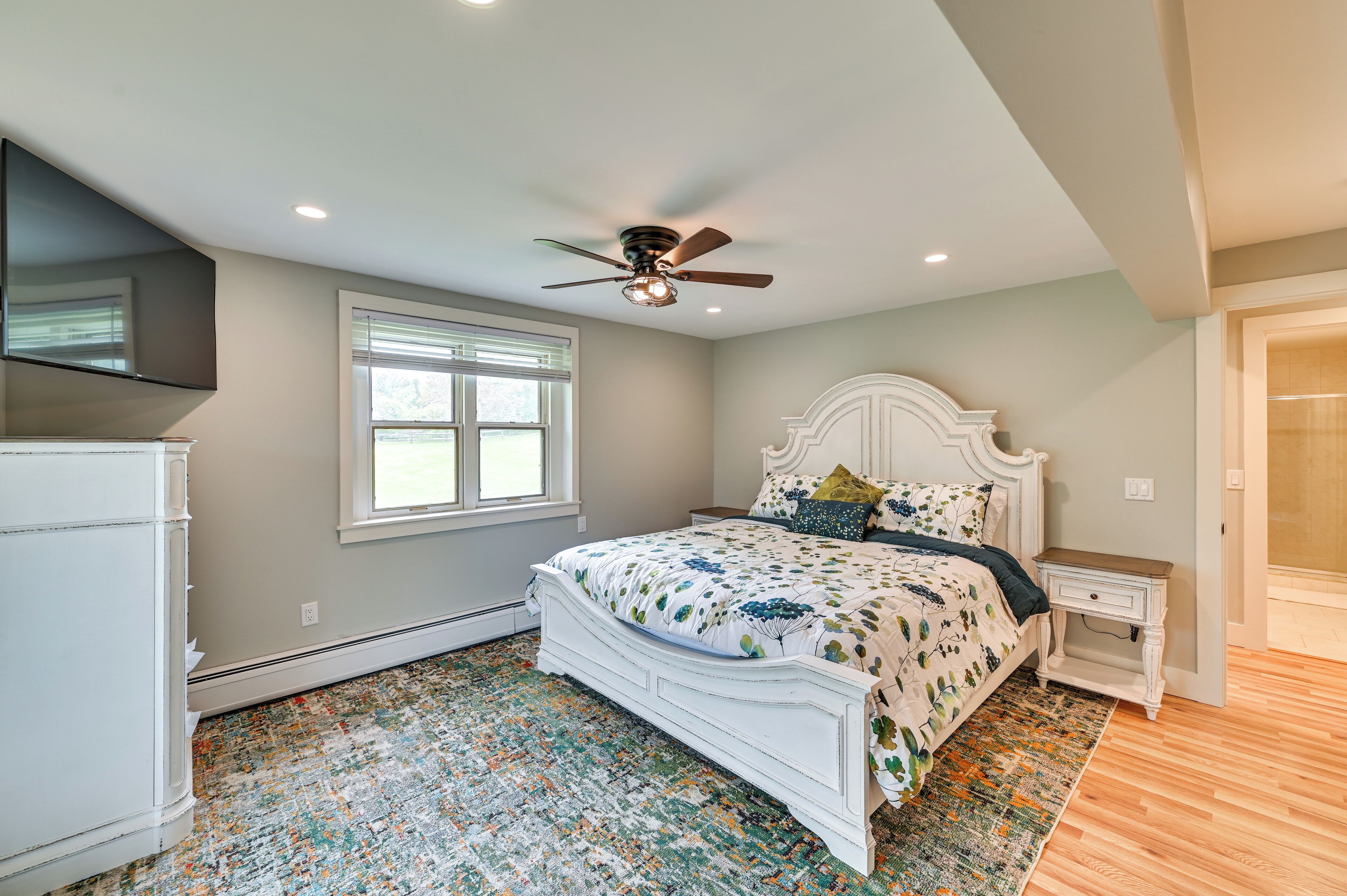 A bedroom with a bed, a ceiling fan, a window, and a white dresser.